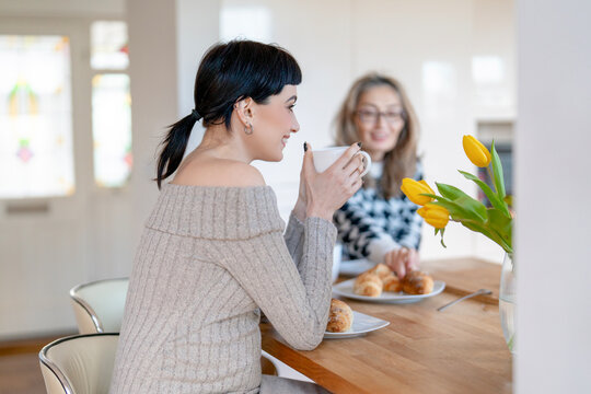 Friends enjoy coffee and croissants in a cozy kitchen with fresh flowers during a sunny morning gathering