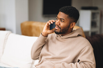 Young man sitting on a couch engages in an important phone conversation while wearing a casual...