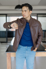 Stylish man wearing casual clothes is looking at his wristwatch while standing in a modern home...