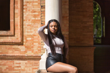 Young, beautiful, African woman, with sweater and leather shorts, eyes closed and hand on her head,...