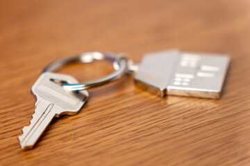 A key attached to a metallic house-shaped keychain on a table. Homeownership, real estate, property...