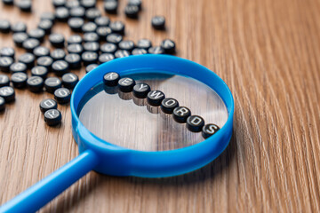 A blue magnifying glass with alphabet beads that spell out KEYWORDS. Searching, optimization, discovery, SEO, data, and online content concept.