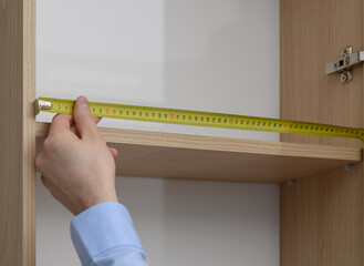 A carpenter makes a custom-made wardrobe, measuring the length of the shelf with a ruler