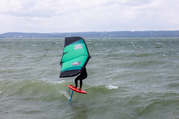 A lone wing foiler sails across a breezy lake, balancing with a green wing above sparkling water on...