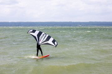 Person doing wing foiling on a lake during windy weather. Focus on movement and sail