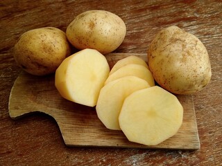 Whole fresh potatoes and slices on a cutting board.