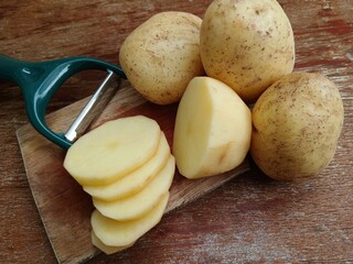 Whole fresh potatoes and slices on a cutting board.