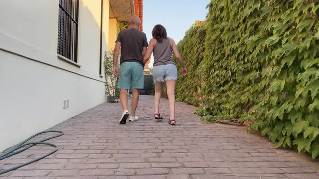 Rear view of young woman with cerebral palsy walking for exercise hand in hand with her supportive elderly father along a suburban sidewalk, symbolizing strength and connection