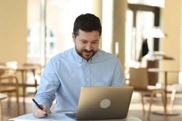 Handsome business owner working with laptop at table in his cafe