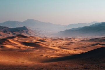 Naklejka premium Soft-focus sunrise over vast, ochre sand dunes and distant, hazy mountains under a pale sky