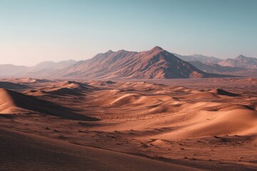 Naklejka premium Expansive desert landscape with rolling sand dunes stretching towards a majestic mountain range under a clear, pale sky