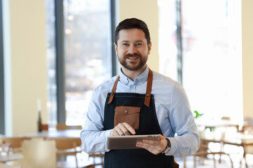 Portrait of smiling business owner with tablet in his cafe