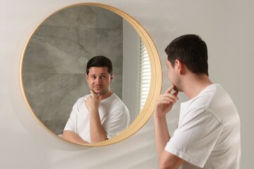 Handsome man looking at himself in mirror indoors