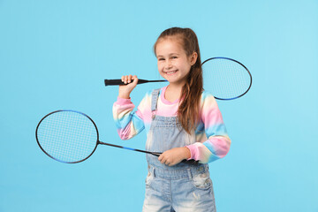 Little girl with tennis rackets on light blue background