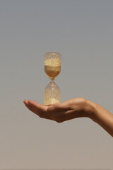 Hand holding hourglass with golden sand under soft sunset light