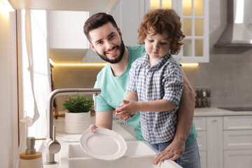 Father and his son washing dishes together in kitchen at home