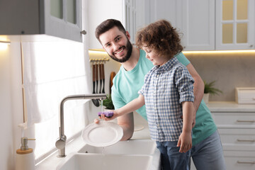 Father and his son washing dishes together in kitchen at home