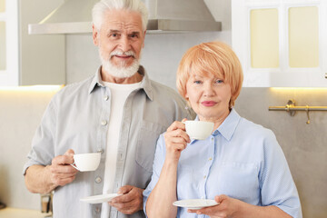 Lovely senior couple with cups of coffee in kitchen