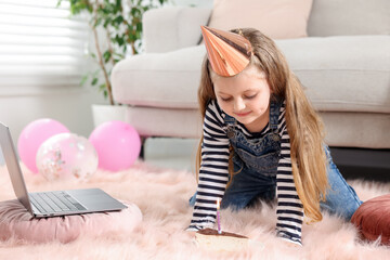Birthday celebration. Little girl with piece of cake having video call via laptop at home