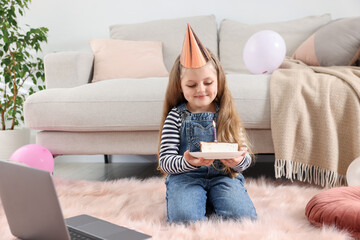 Birthday celebration. Little girl with piece of cake having video call via laptop at home