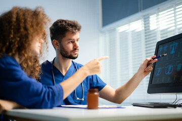 Male doctor explains health scan results to female patient using a computer screen. Concept of diagnosis, health tech, medical consultation