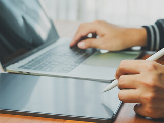 Person using digital pen on tablet with laptop keyboard in background, showing modern technology...