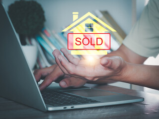 Person using laptop with digital house icon and sold sign, symbolizing real estate transaction and...