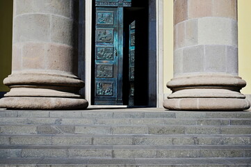 the entrance gate of the Eger Basilica in Neoclassical style with heavy stone columns and copper plated entrance doors. beautiful Relief tables of mythological scenes. Doric column base. stone steps