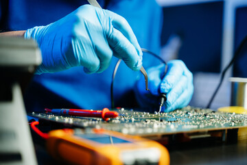 Electronics technician soldering a green PCB with precision in a modern lab, wearing gloves and...