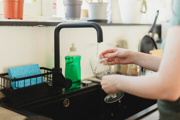 Cropped hands of woman washing dishes in kitchen sink at home. Daily chores, dish washing and home hygiene concept. 