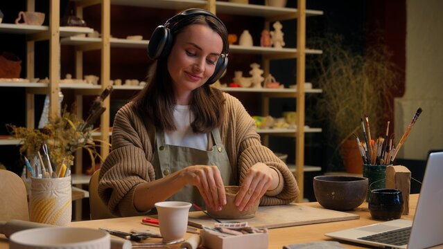 Caucasian relaxed woman girl female potter modeling clay process in workshop pottery hobby smiling sculptor designer listen music audio in headphones ceramics art therapy creating pot handmade craft - Powered by Adobe