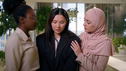Upset sad frustrated crying Asian girl in office dismissed lost job crisis women business colleagues African Muslim businesswomen support help calm multiracial friendship community supportive unity