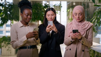 Three diverse multiracial business women addicted mobile phones businesswomen African Asian Muslim girls addiction gadgets in office females using smartphones messaging internet co-workers ignoring