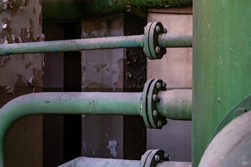 rusty green pipes with flanges in an abandoned industrial facility. Peeling walls and dark...
