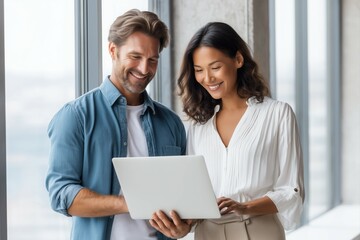 Handsome Caucasian man with brown hair and a blue shirt is showing his laptop screen to a beautiful Asian woman in a white blouse.
