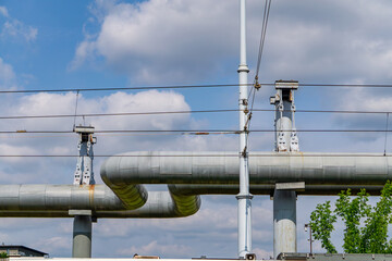 Overhead district heating pipes on supports crossing an urban area, with traction poles and wires...
