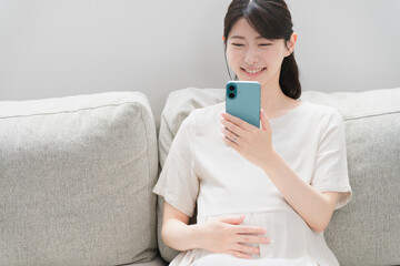 ソファーでスマートフォンを操作する妊婦　ライフスタイルイメージ