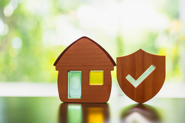 Wooden house model and real estate insurance ideas, and small shield icon. Housing insurance against impending loss and fire, building fire insurance concepts.