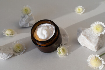 Jar of cosmetic cream on stone table decorated with flowers. Beauty, spa and skincare lifestyle aesthetic concept top view.