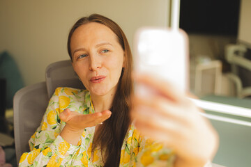 Young woman wearing a white dress with a lemon print taking a selfie with her smartphone. POV shot...