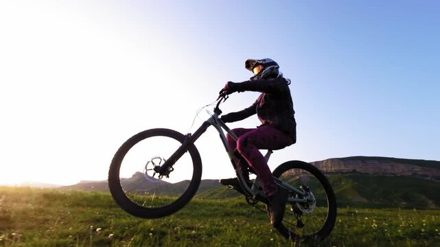 Young male rider doing wheelie on his bicycle in slow motion in mountains. Aerial view from fpv drone with epic rocky mountains