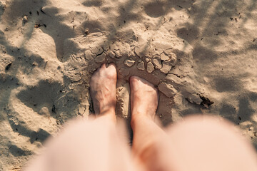 Close top view of female feet partially covered in sand on a beach at sunset