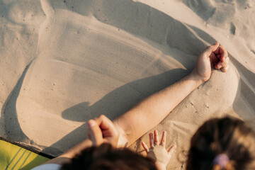 Father’s hand smoothing sand on the beach while child draws with a stick. A warm and tender...