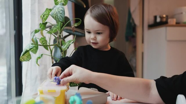 Mother playing with her daughter with dinosaur toys at the children's table. Happy family, time together. Child development, playtime concept. Little child playing with parents.