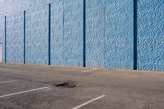 Minimal urban street corner with intense blue wall and shadows, suggesting abstraction and spatial emptiness in city design