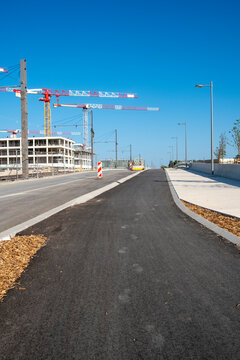 Urban road infrastructure in development with visible construction cranes and freshly paved lanes, under clean morning light