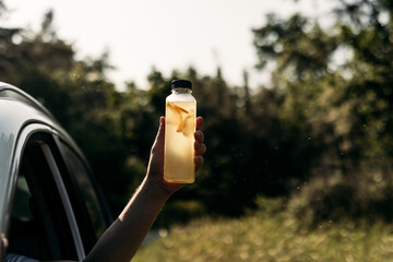 Lemonade in the golden sun — a bottle held from a car window on a summer afternoon evokes...