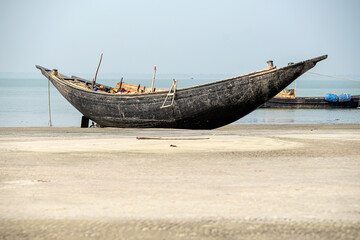 Old fishing boat rests on a sandy shore near the coast, reflecting the calmness of the sea on a...