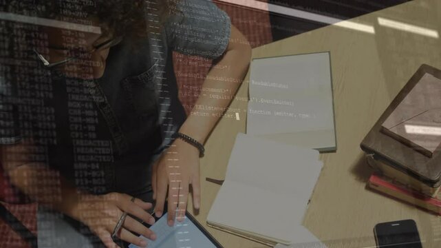 Man tapping blue tablet and referencing notebook while reviewing code overlay for tech development