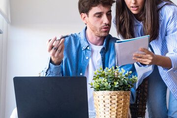 Young couple sitting at a desk at home discussing their family budget. Focused expressions while...
